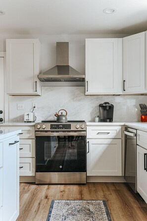 Une cuisine moderne avec des armoires blanches, une cuisinière en acier inoxydable et un four encastré.