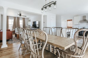 Ein Essbereich mit einem Holztisch, weißen Stühlen, einem Deckenventilator und einer Küche im Hintergrund.