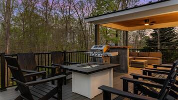 Een terras buiten met een barbecue, zitgedeelte en uitzicht op het omliggende bos.