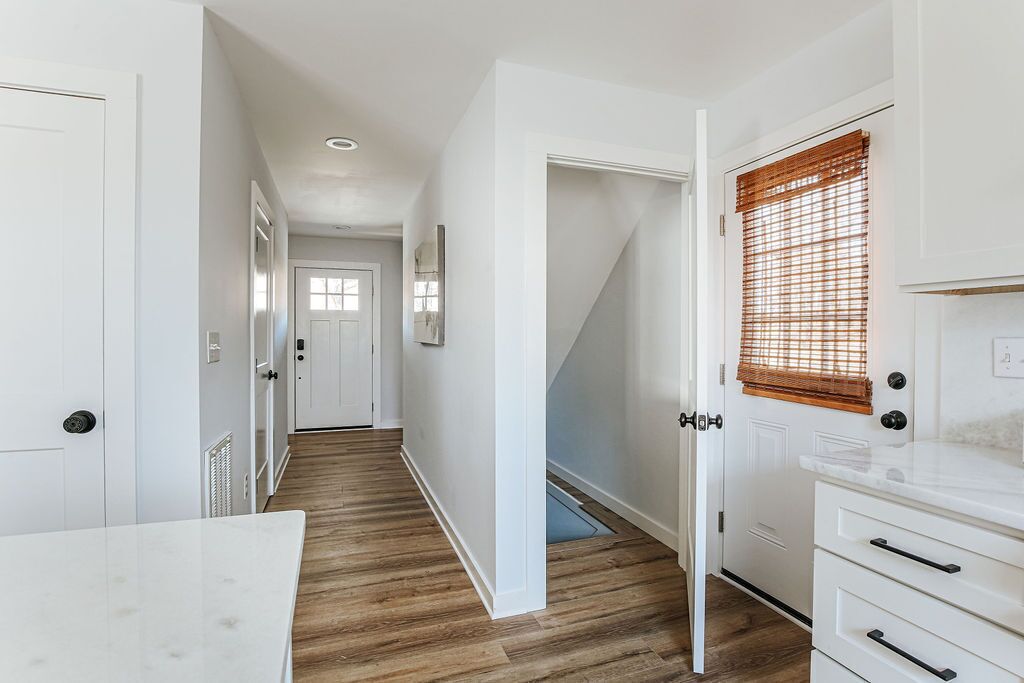 Un couloir aux murs blancs, au plancher en bois et aux meubles de rangement blancs.