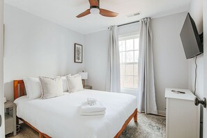 Une chambre d’hôtel comprenant un lit, un ventilateur de plafond, une fenêtre avec des rideaux, un téléviseur à écran plat et un petit meuble de rangement.