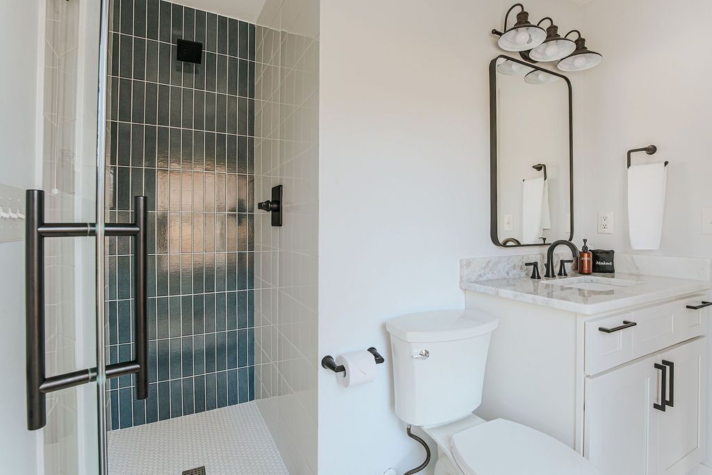 Une salle de bain avec une douche à parois de verre, des toilettes blanches, un lavabo avec un miroir et un porte-serviettes.