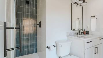 Une salle de bain avec une douche à parois de verre, des toilettes blanches, un lavabo avec un miroir et un porte-serviettes.
