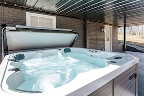 Ein Whirlpool unter einer überdachten Terrasse, im Hintergrund eine Backsteinmauer und eine Tür.