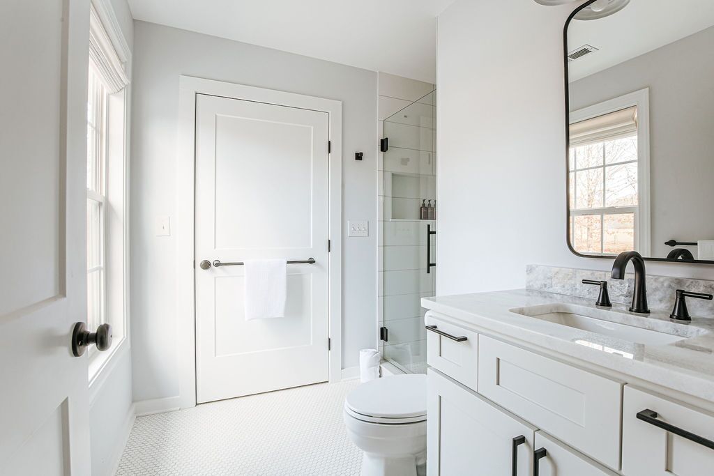 A modern bathroom with white fixtures, a glass shower enclosure, and a large mirror.