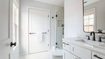 A modern bathroom with white fixtures, a glass shower enclosure, and a large mirror.