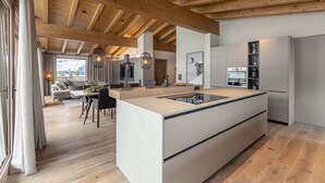 A modern kitchen with a central island, wooden beams on the ceiling, and a dining area with a sofa and table. - Apartment in Tyrol Near ski Area (Westendorf)