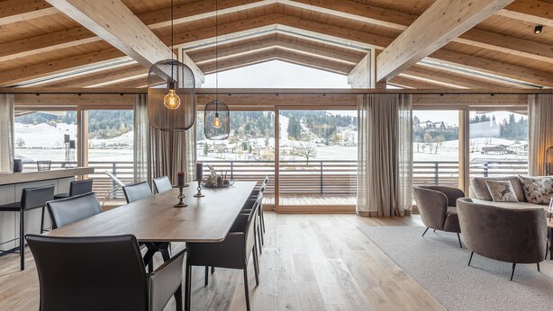 A spacious dining area with a long wooden table and chairs, large windows offering a view of a snowy landscape, and a modern chandelier. - Apartment in Tyrol Near ski Area (Westendorf)