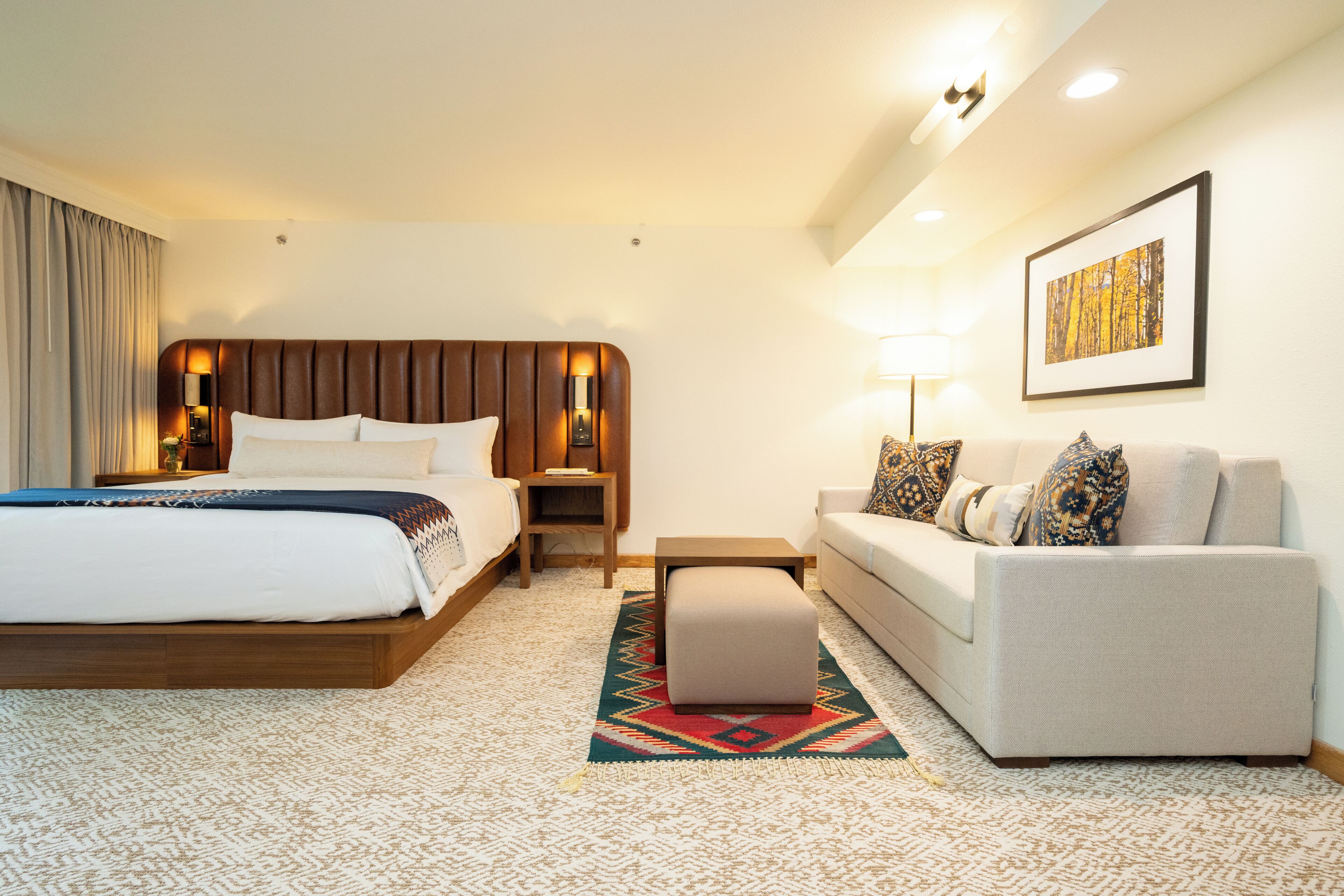A hotel room with a large bed, a sofa, a small table, and a wall-mounted lamp.