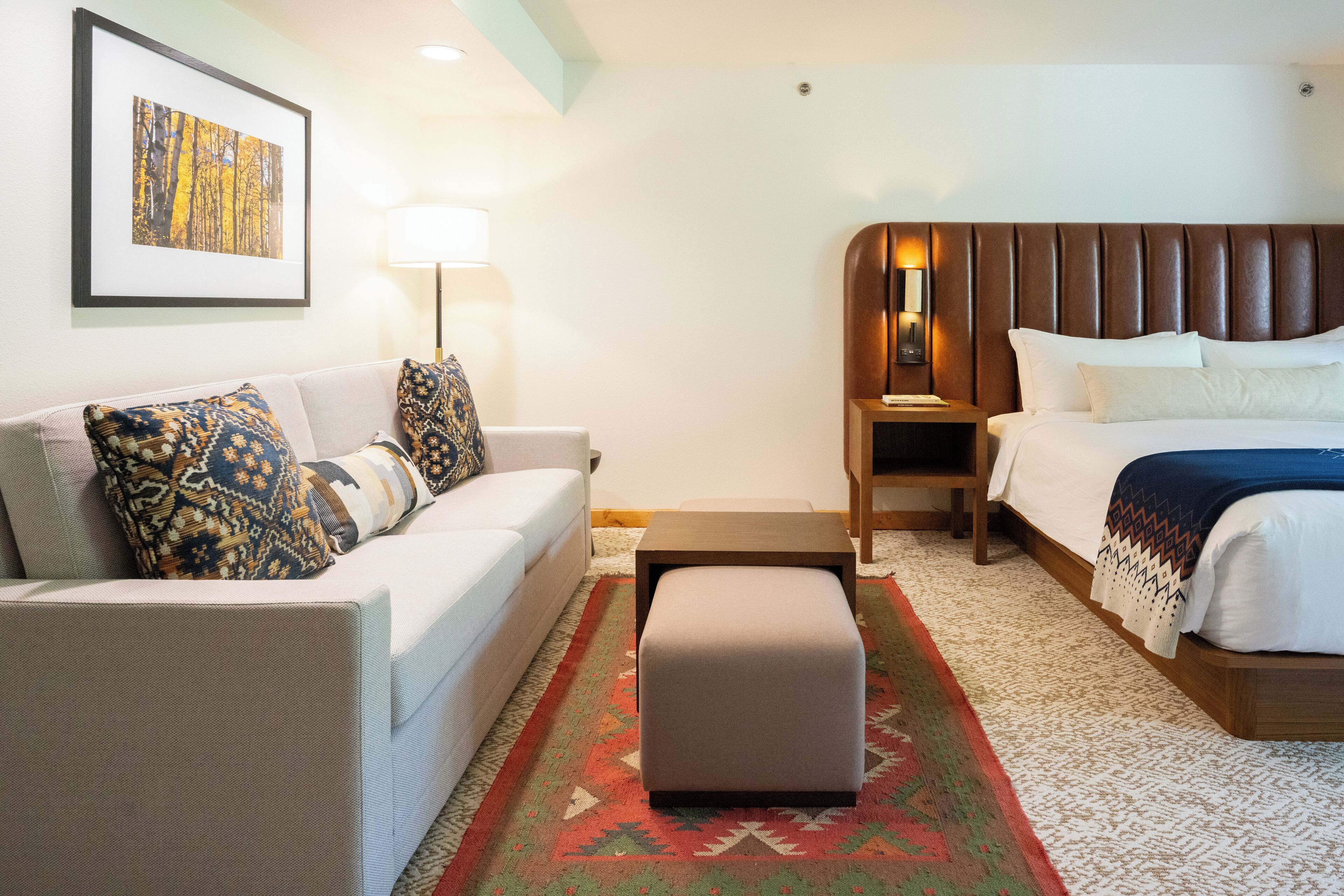 A hotel room with a bed, a sofa, a small table, a lamp, and a rug.