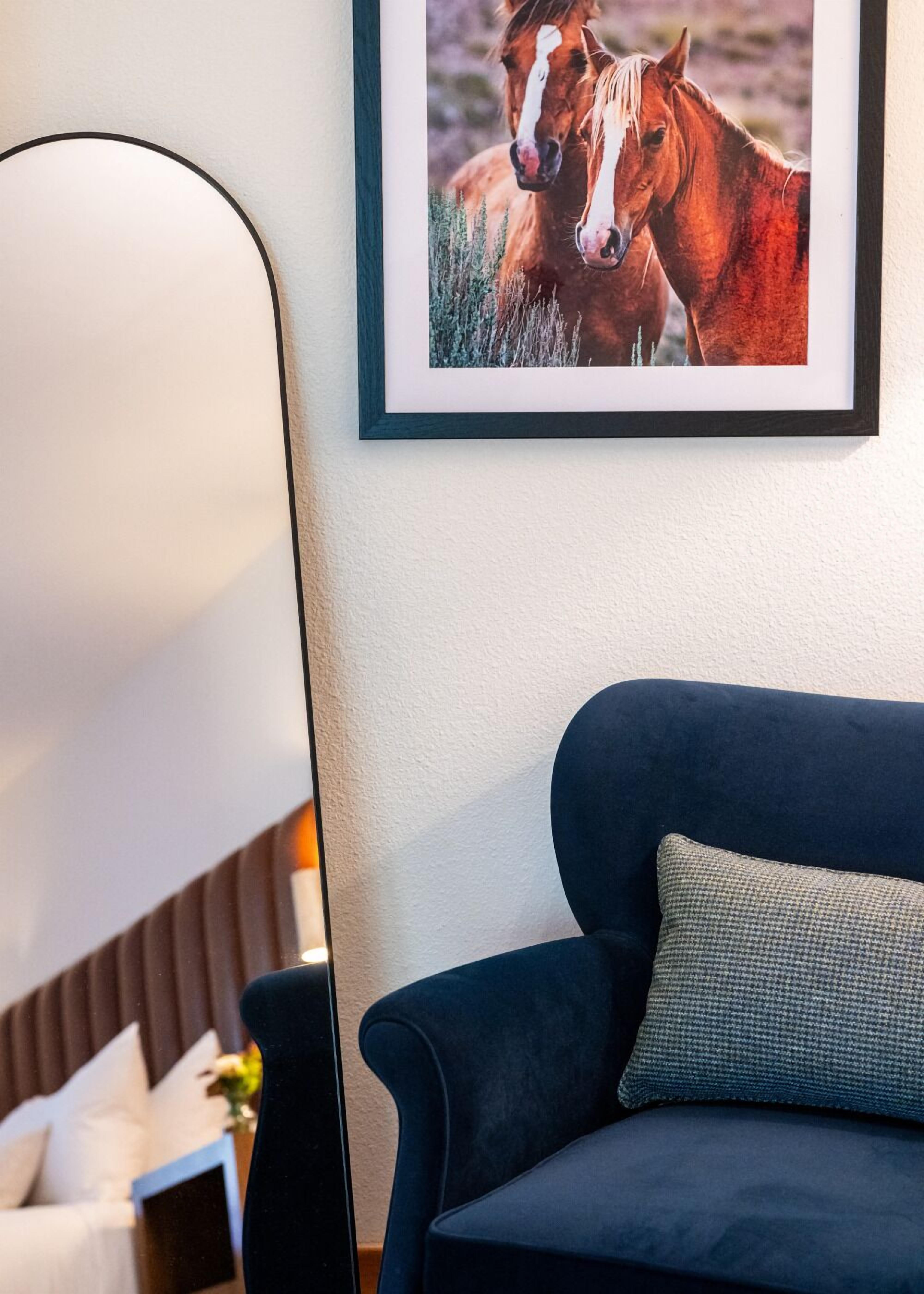Et indrammet billede af to heste hænger på væggen over en mørkeblå sofa med en struktureret pude.