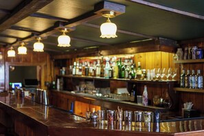 A bar with wooden beams, hanging light fixtures, and shelves stocked with bottles and glasses. - Rock Creek Resort (Red Lodge)
