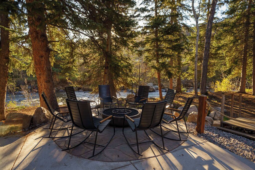 A fire pit surrounded by chairs in a forested area.
