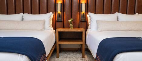 A hotel room with two beds, a wooden nightstand with a vase, and wall-mounted lamps.
