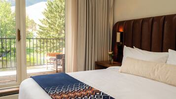 A hotel room with a large bed, a wooden headboard, a nightstand with a lamp, a window with curtains, and a balcony with a chair.