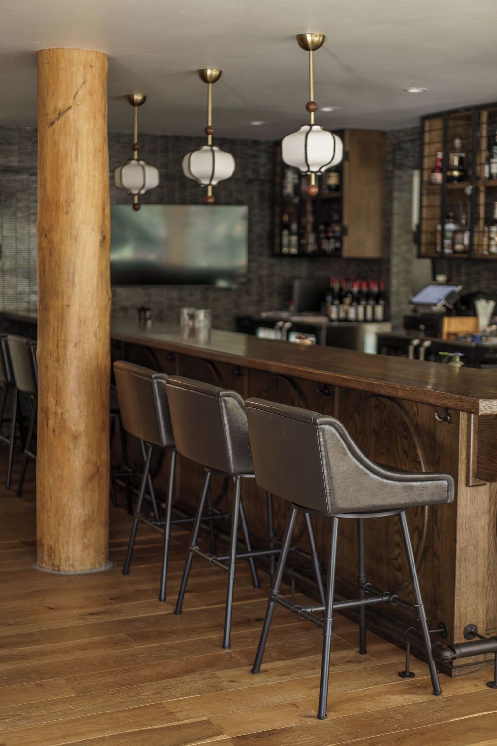 A bar area with wooden stools, a bar counter, and hanging pendant lights.