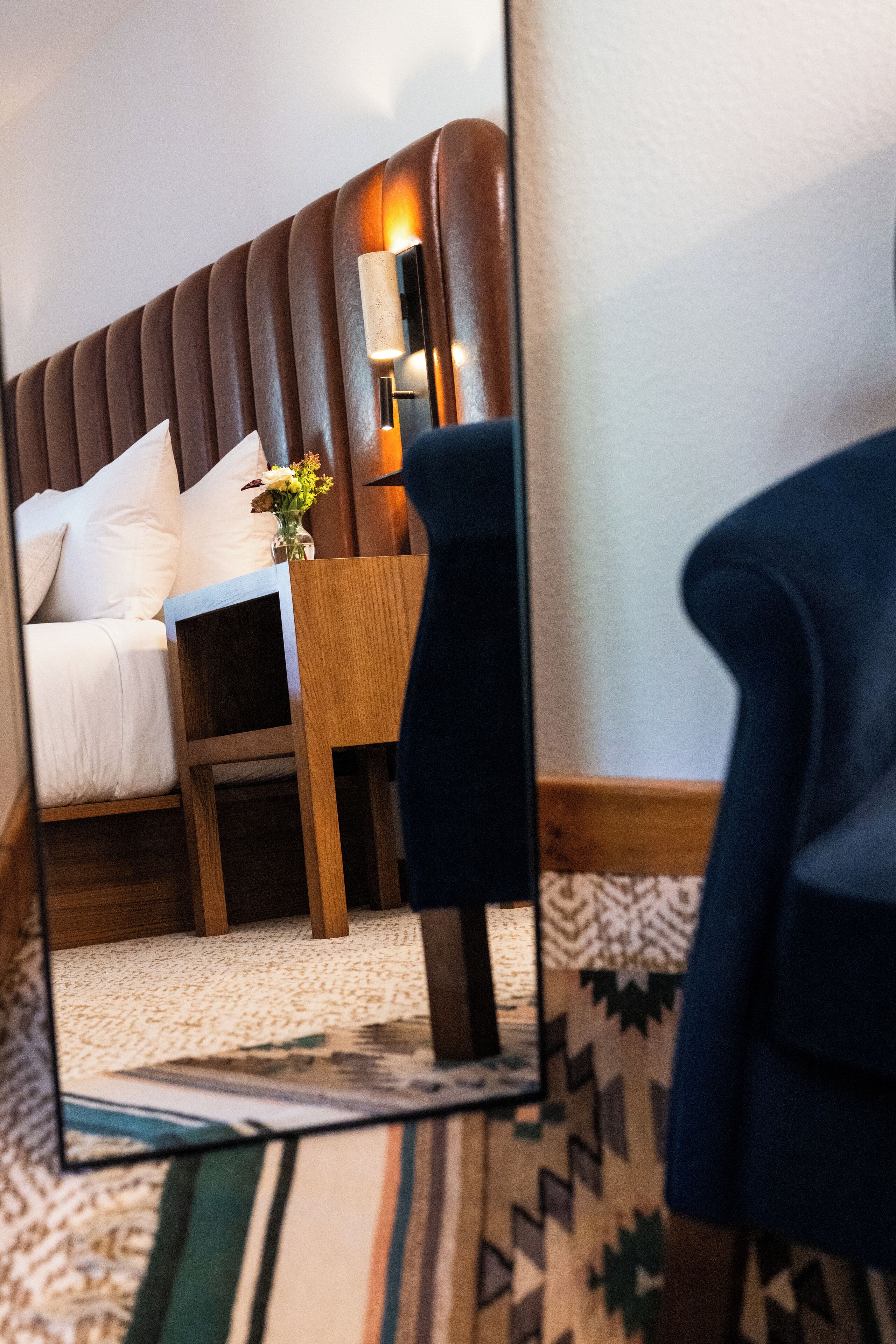 Une chambre à coucher avec un lit, une table de chevet, une lampe et un miroir qui reflète la pièce.