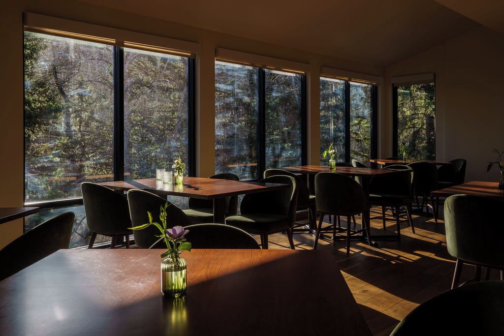 Un espace repas doté de grandes fenêtres, de tables et de chaises en bois.