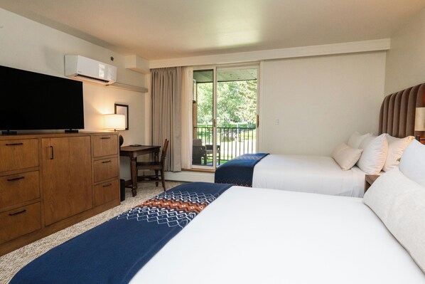 Habitación de hotel con dos camas, un escritorio, televisión y puerta corrediza de vidrio al exterior.