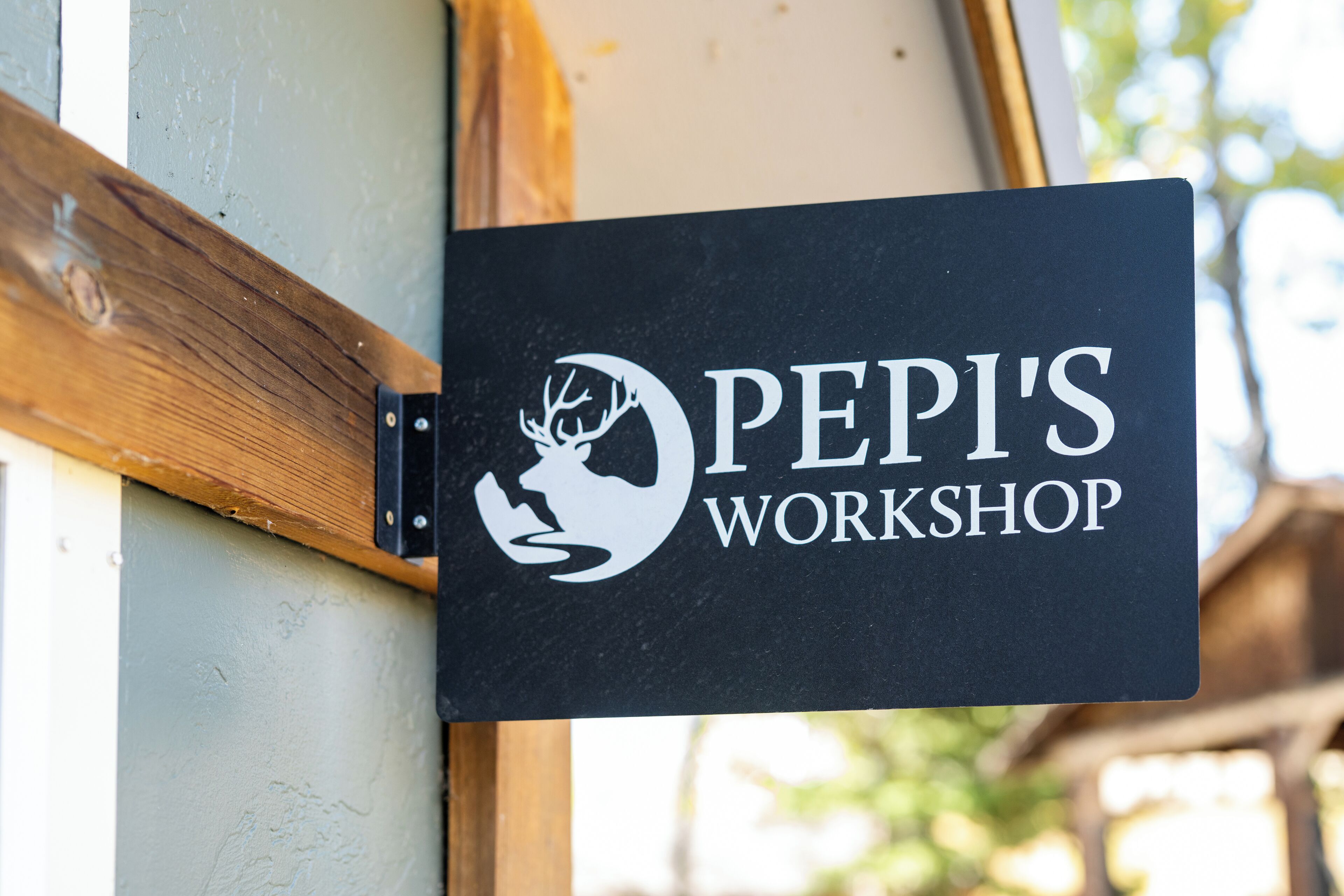A sign for "PEPI'S WORKSHOP" with a logo, mounted on a wooden structure.