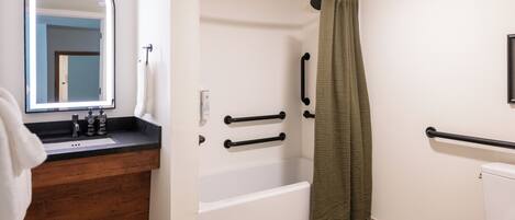 Een badkamer met een houten wastafelmeubel, een witte badkuip, een groen douchegordijn en een wit toilet.