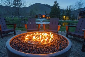 A fire pit with chairs around it, a pond, and a lodge in the background. - Rock Creek Resort (Red Lodge)