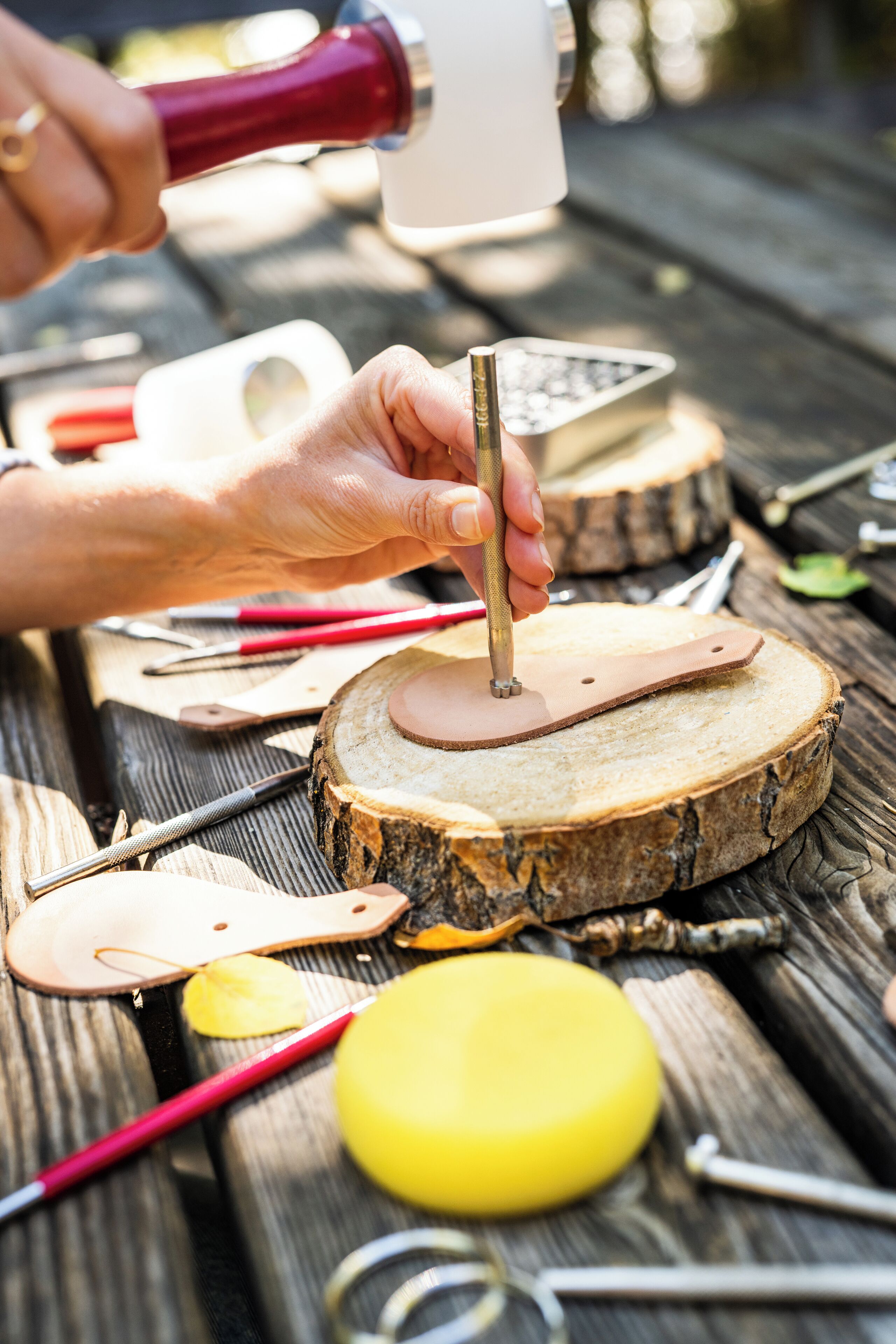 Una persona trabajando en una pieza de cuero sobre una superficie de madera, con herramientas y materiales.