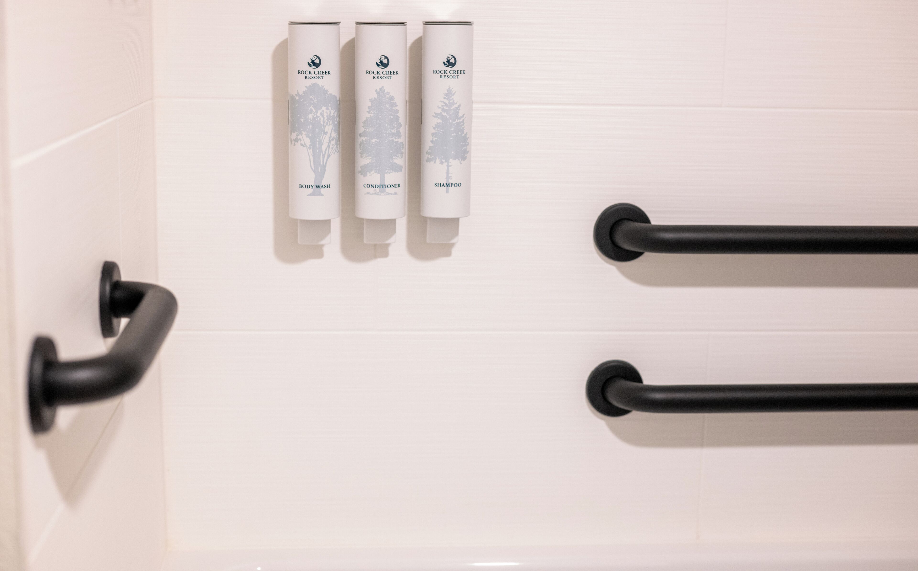 A bathroom with three toiletries: body wash, conditioner, and shampoo, all from Rock Creek Resort.