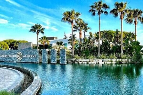 A swimming pool with palm trees and a stone wall with the text "Valet de Chambre".