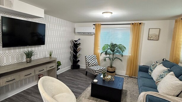 Una sala de estar moderna con un televisor de pantalla plana, un sofá, una silla, una mesa de centro y una alfombra estampada.