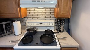 Una cocina con estufa blanca, dos sartenes, una olla y un dispensador de toallas de papel.