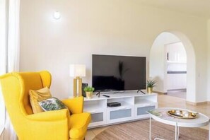 Ein modernes Wohnzimmer mit einem gelben Sessel, einem Flachbildfernseher auf einer weißen Unterhaltungsanlage und einem kleinen Couchtisch mit Tablett.