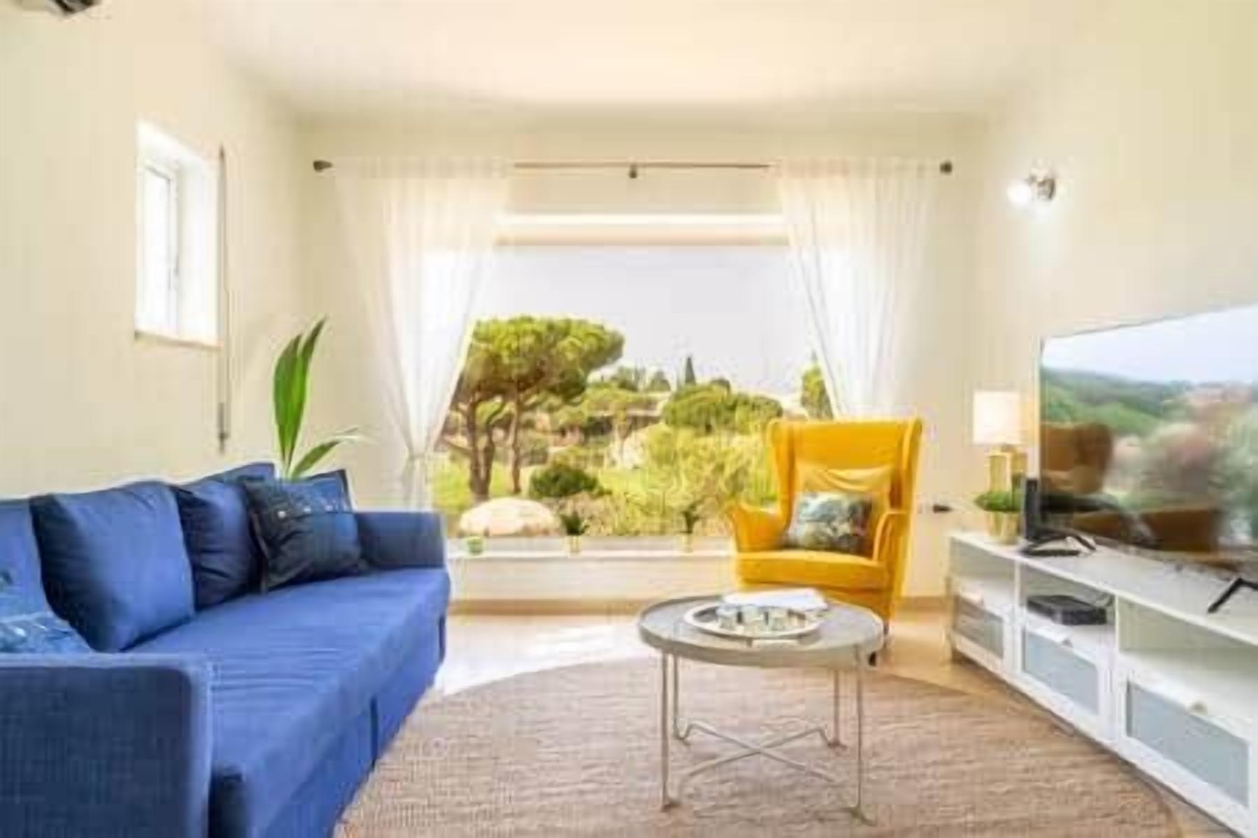Un soggiorno con divano, poltrona, televisore e vista sul verde.