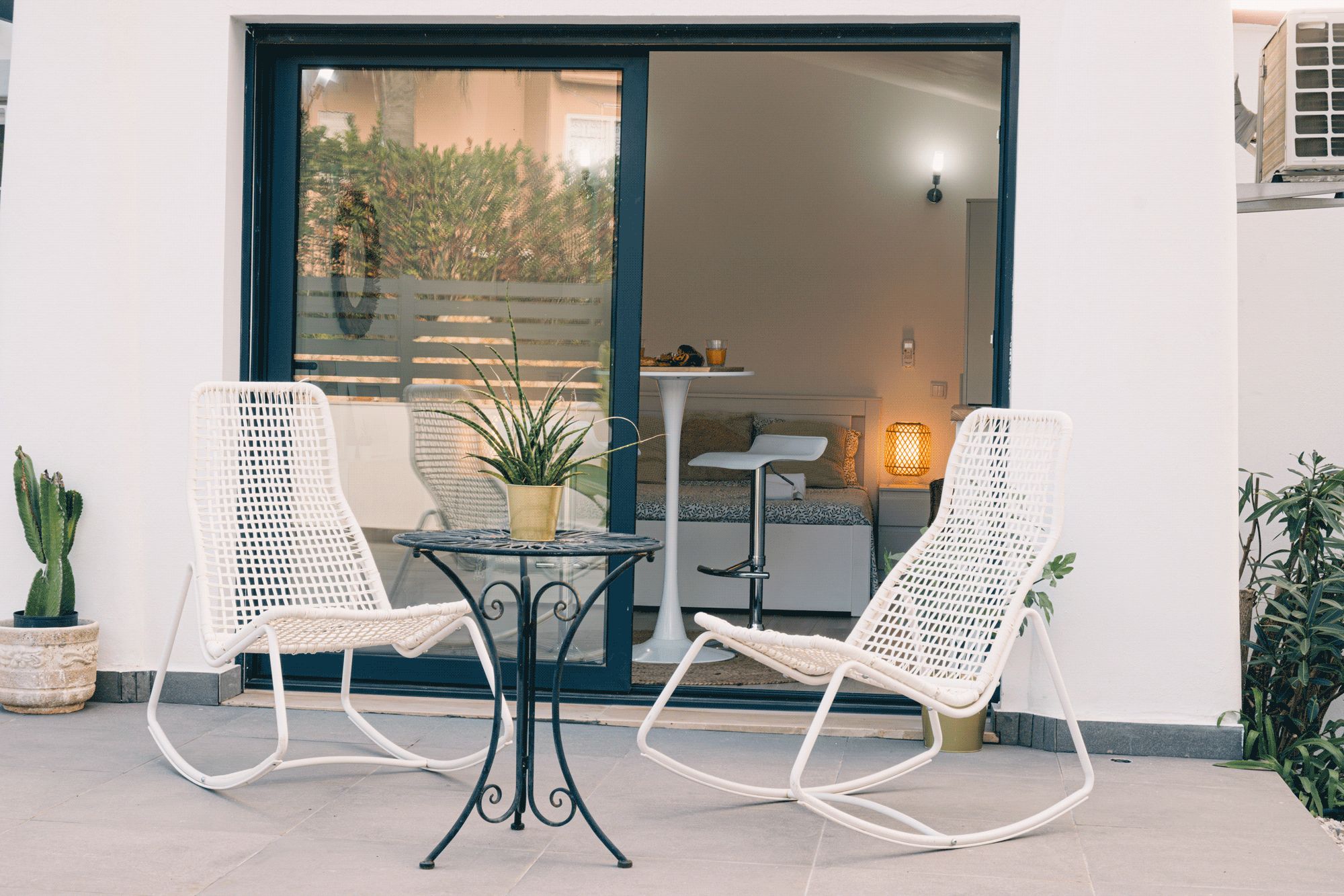 Une terrasse avec deux chaises en osier blanches, une petite table ronde et un pot de fleurs.