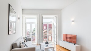A modern living room with a sofa, a coffee table, and a TV. There are two large windows with a view of buildings outside. - GuestReady - A peaceful ambience in Porto (Porto)