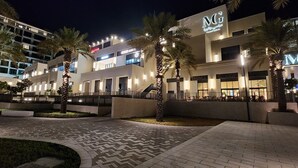 Un hotel moderno con un llamativo logotipo de MG, palmeras y un área de entrada bien iluminada.