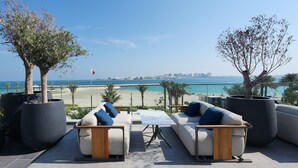 Una terraza con asientos al aire libre, grandes macetas con plantas y vistas a la playa y al horizonte de la ciudad.