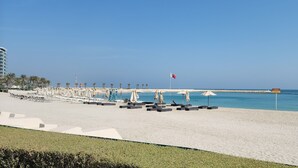 Una playa con tumbonas y sombrillas, una bandera y un muelle.