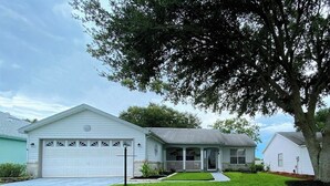A single-story house with a front porch, a garage, and a well-maintained lawn. - Renovated! Between Two Squares with Golf Cart ! (The Villages)