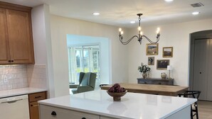 A modern kitchen with a central island, wooden cabinets, and a chandelier. - Renovated! Between Two Squares with Golf Cart ! (The Villages)