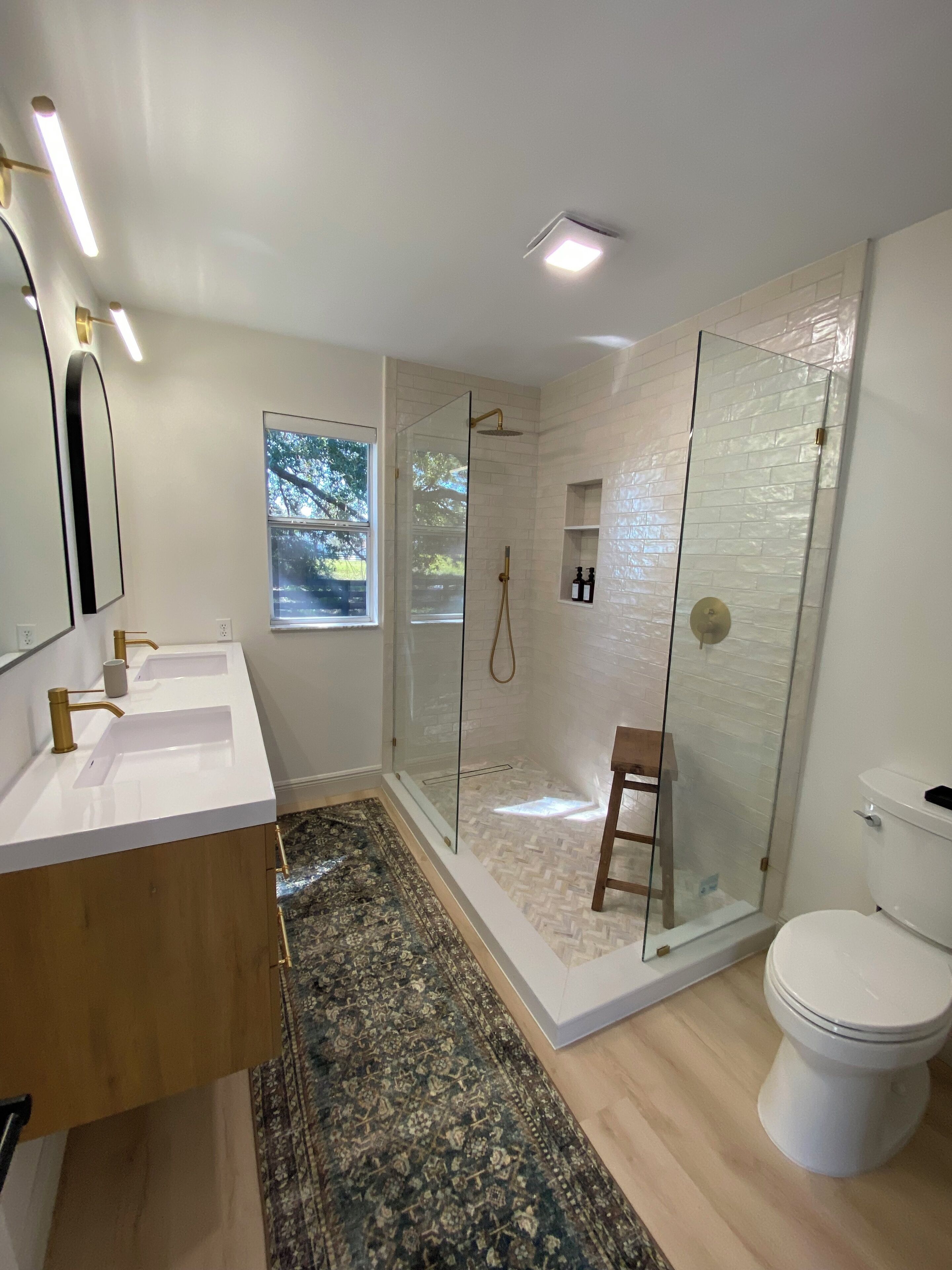 Un baño moderno con ducha de mampara de vidrio, inodoro blanco y un espejo grande.