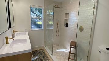 Un baño moderno con ducha de mampara de vidrio, inodoro blanco y un espejo grande.