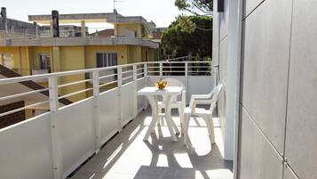 A balcony with a table and chairs, a potted plant, and a view of neighboring buildings.