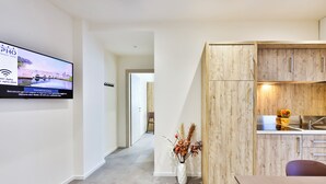 A modern kitchen with wooden cabinets and a built-in stove, a dining area with a table and chairs, and a TV mounted on the wall displaying a welcome message. - Apho Apartment-Hotel (Rimini)