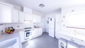 A modern kitchen with white cabinets, a gas stove, an oven, a refrigerator, and a small dining area with a stool.