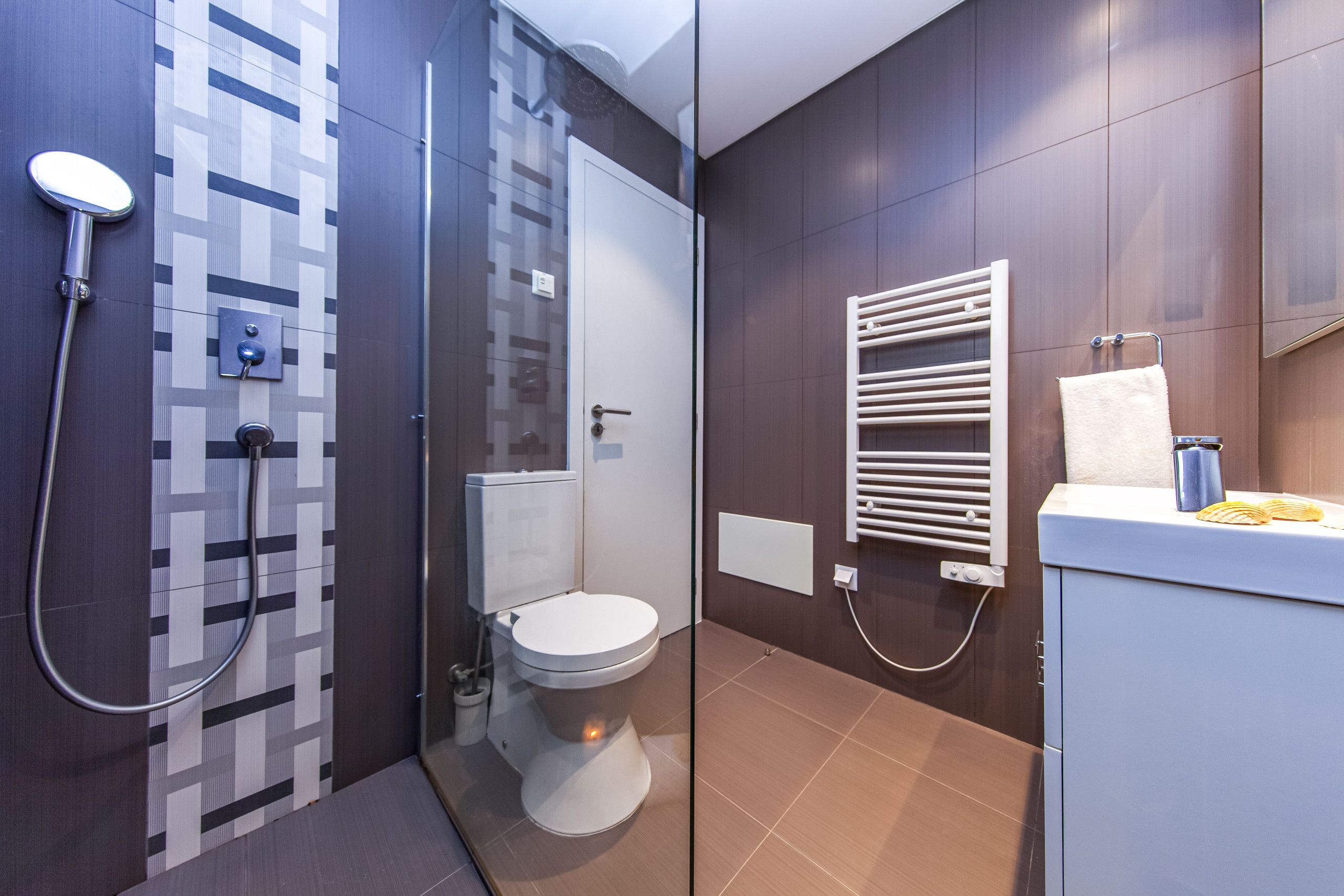 Un baño moderno con cabina de ducha de vidrio, inodoro, toallero y tocador con espejo.