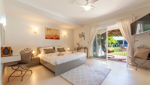 A bedroom with a bed, a desk, a chair, a ceiling fan, and a view of the outdoors.