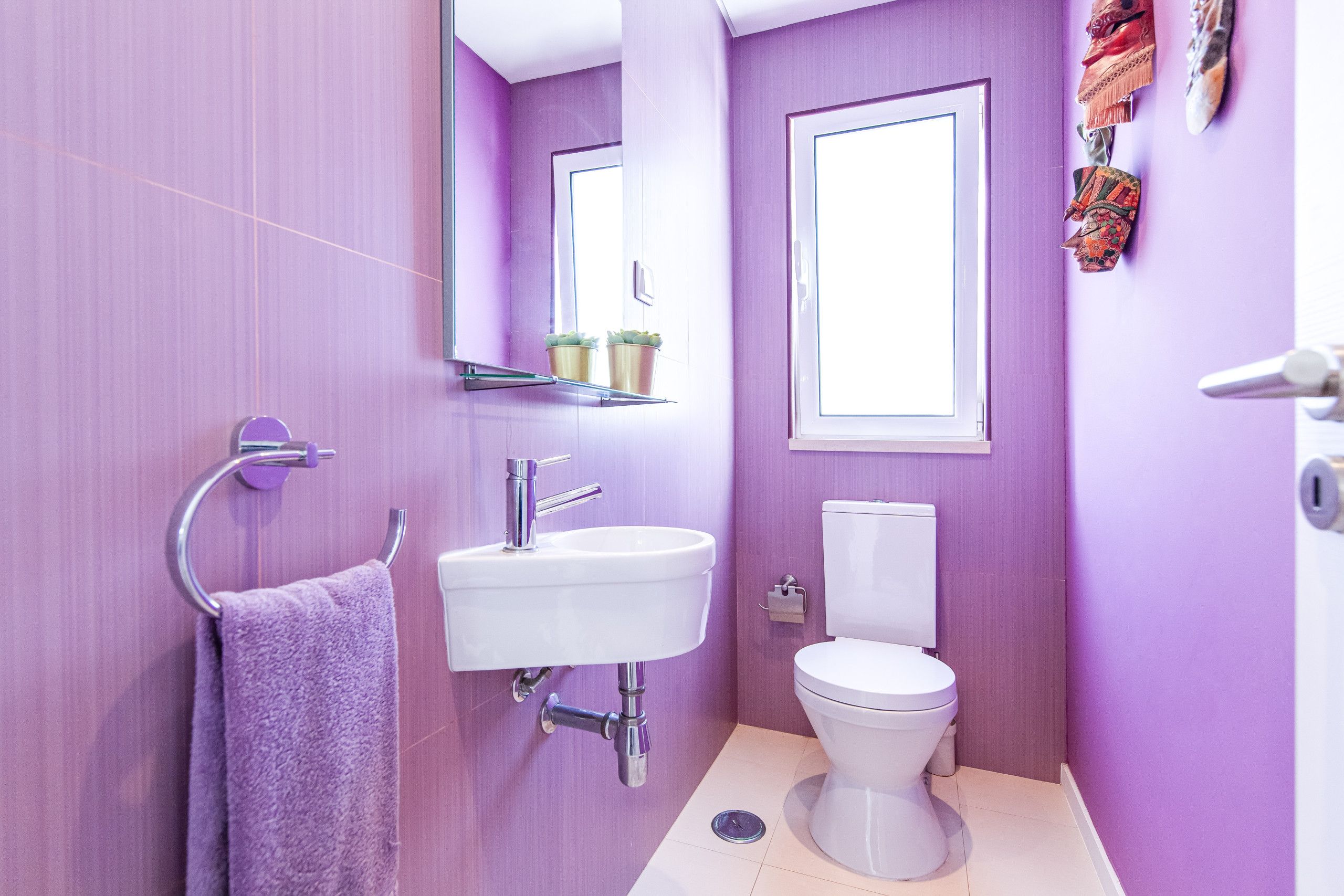 A bathroom with a purple wall, a white sink, a toilet, and a mirror.