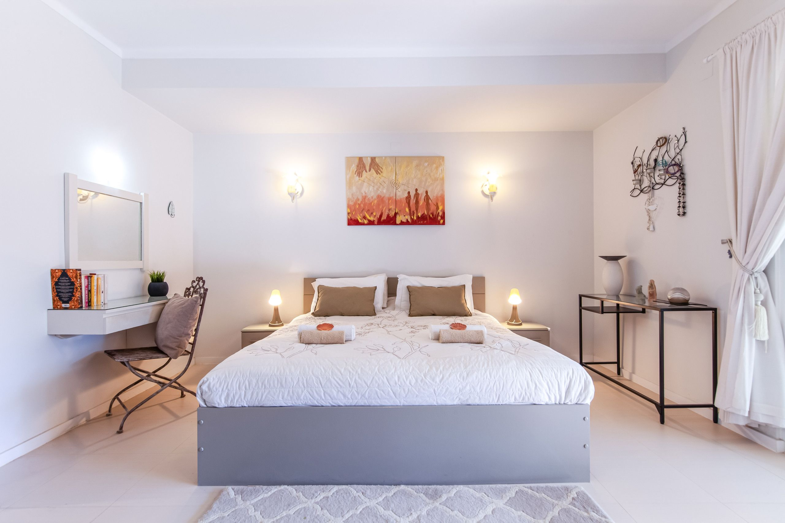 A modern bedroom with a large bed, bedside tables, a desk, and a chair.