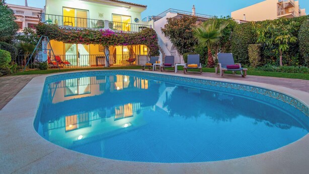 A swimming pool with lounge chairs, a staircase, and a building with balconies.